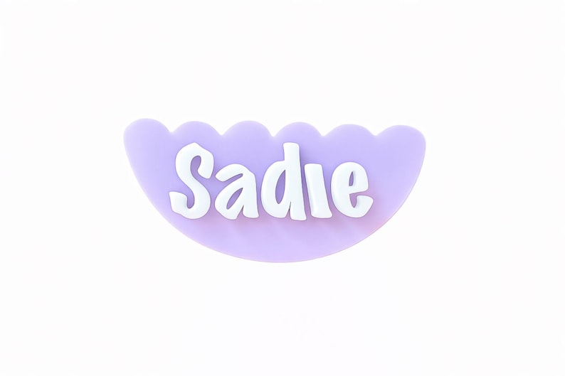 May include: A light purple, scalloped-edge name tag with the name "Sadie" in white, bold letters. The name tag is a half-circle shape, and the background is plain white.