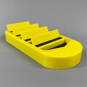 Può includere: Un vassoio organizer in plastica giallo brillante dotato di quattro fessure a gradini con strisce di gomma nera alla base di ogni sezione. L'unità presenta un bordo anteriore arrotondato e un design a gradini per riporre piccoli oggetti.