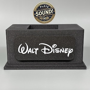 May include: A black sound box with the words "Walt Disney" printed on the front. A gold circular sticker with the words "Plays Sound!" is above the box.