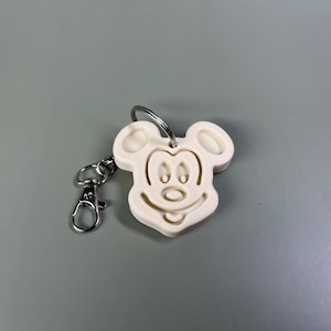 Pode incluir: Chaveiro de pl&aacute;stico branco com um design de cabe&ccedil;a do Mickey Mouse. O chaveiro tem um anel de metal prateado e um fecho de metal prateado.