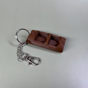 Pode incluir: Um chaveiro de barco de madeira marrom com uma corrente e um fecho prateados.