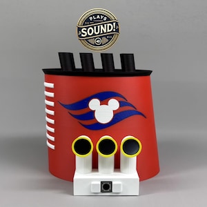 May include: A red, white, and black decorative object resembling a ship's smokestack, featuring the iconic Mickey Mouse silhouette and the text "PLAYS SOUND!". The object has three yellow-rimmed speakers and a small speaker on the base.