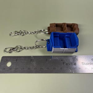 Pode incluir: Dois chaveiros com assentos de carro em miniatura. Um &eacute; azul com uma faixa branca e o outro &eacute; marrom. Ambos est&atilde;o presos a correntes prateadas com fechos prateados.