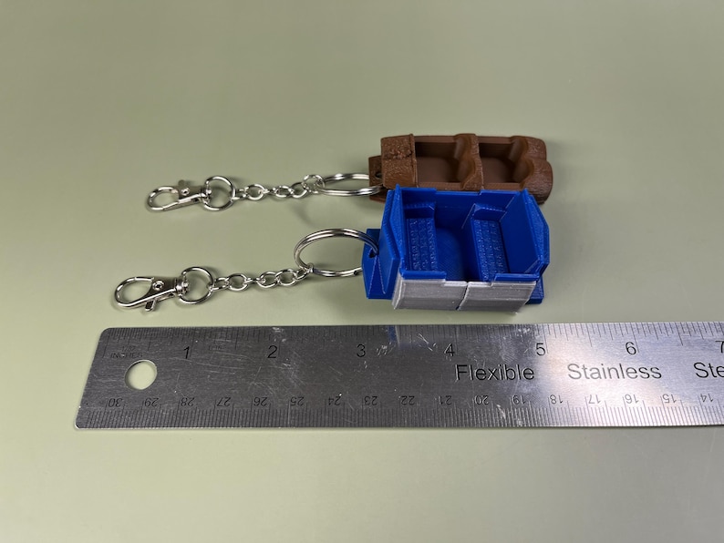 Pode incluir: Dois chaveiros com assentos de carro em miniatura. Um &eacute; azul com uma faixa branca e o outro &eacute; marrom. Ambos est&atilde;o presos a correntes prateadas com fechos prateados.