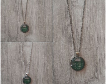 May include: A silver chain necklace with a round green glass pendant. The pendant has a white crown and the text "Weasley is our King" written on it.