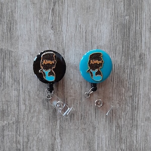 May include: Two retractable badge holders with a silhouette of a person's head and the word "Always" in gold lettering. One badge holder is black with a blue silhouette and the other is blue with a black silhouette.