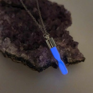 May include: A silver chain necklace with a blue glow-in-the-dark hourglass pendant.