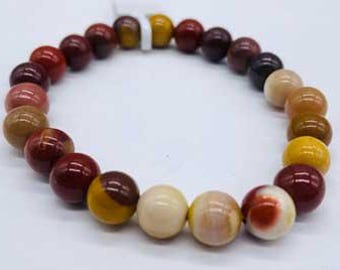 May include: A beaded bracelet featuring a variety of polished, round gemstones in shades of red, brown, yellow, and cream. The beads are strung together, forming a circular shape against a white background.