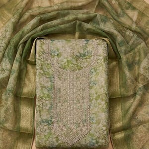 May include: A three-piece clothing set featuring a rectangular tunic with a green and white floral print and a central panel of silver embroidery, a matching sheer green floral dupatta with gold borders, and a solid dark green fabric piece.