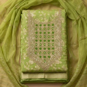 May include: A lime green fabric piece featuring a white floral pattern and a central rectangular panel with gold embroidery, green sequins, and small green beads. It is accompanied by a matching sheer lime green scarf with gold metallic stripes.