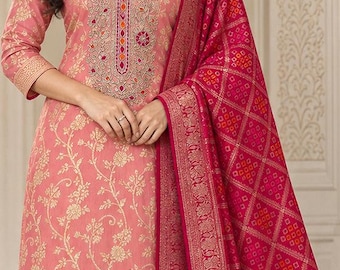 May include: A peach-colored straight-cut kurta featuring a gold floral pattern, three-quarter sleeves, and a detailed embroidered neckline. It is paired with matching peach trousers and a vibrant magenta dupatta with a gold border and geometric print.