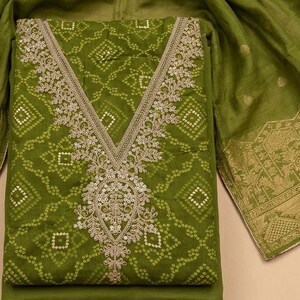 May include: An olive green fabric set featuring a tunic with a V-neckline adorned with intricate gold embroidery and sequins. The fabric displays a repeating geometric pattern of small white dots. A matching olive green shawl with gold borders.