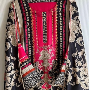 May include: A pink and black patterned dress with gold and silver embellishments. The dress has a round neckline and long sleeves. The fabric is a blend of silk and cotton.