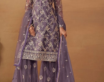 May include: A lavender-colored three-piece outfit consisting of a long-sleeved tunic, wide-leg trousers, and a sheer dupatta. The tunic and trousers feature intricate gold floral embroidery and delicate mesh overlays with a scalloped hemline.