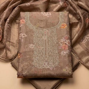 May include: A taupe-colored fabric piece featuring a floral print with orange and white blossoms. The center panel displays intricate silver beadwork and embroidery around the neckline and down the front, accompanied by a matching sheer floral scarf.