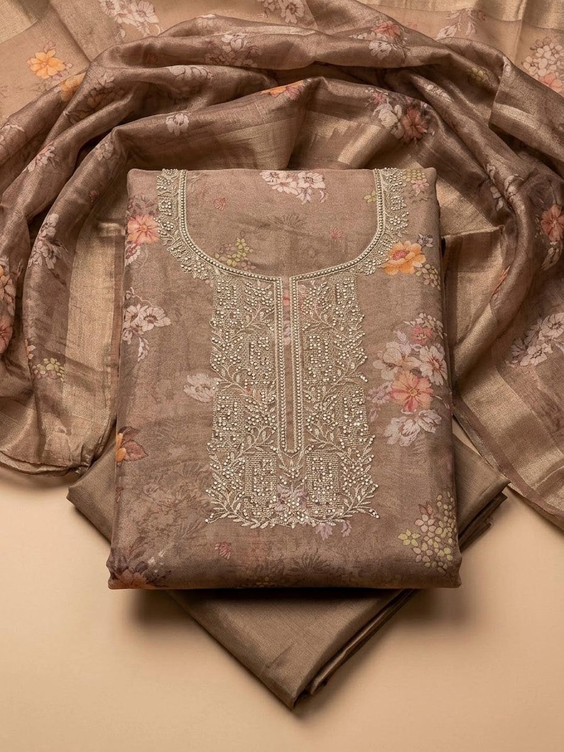 May include: A taupe-colored fabric piece featuring a floral print with orange and white blossoms. The center panel displays intricate silver beadwork and embroidery around the neckline and down the front, accompanied by a matching sheer floral scarf.