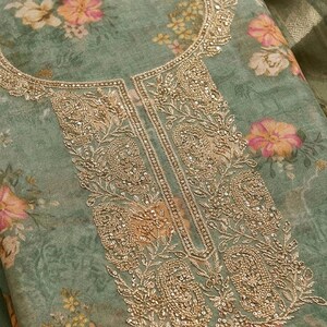 May include: A sage green fabric featuring a floral print with pink and yellow flowers. The neckline and front panel are decorated with intricate gold embroidery, including paisley motifs and small metallic sequins throughout the design.