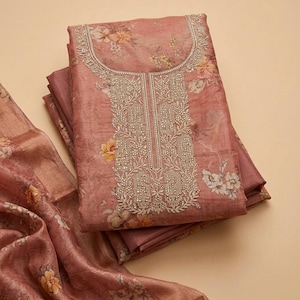 May include: A folded dusty rose fabric garment featuring a floral print in shades of yellow and white. The neckline and front panel are decorated with intricate silver embroidery and small metallic beads, paired with a matching floral fabric piece.