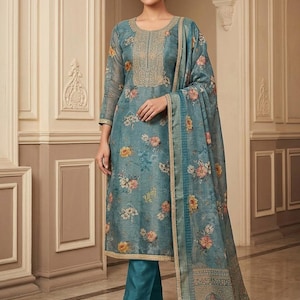 May include: A blue floral print long-sleeved tunic with a round neckline featuring gold embroidery, paired with solid teal trousers and a matching blue floral print dupatta with a gold border. The ensemble is crafted from a sheer, textured fabric.