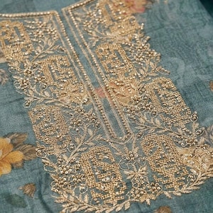May include: A teal fabric garment featuring an intricate gold metallic embroidery pattern around the neckline. The embroidery consists of dense geometric shapes, floral motifs, and small beads. The base fabric has a muted floral print.