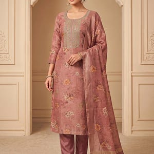 May include: A dusty rose three-piece ensemble featuring a knee-length tunic with three-quarter sleeves, floral patterns, and intricate gold embroidery around the neckline, paired with matching solid trousers and a coordinating floral print dupatta.