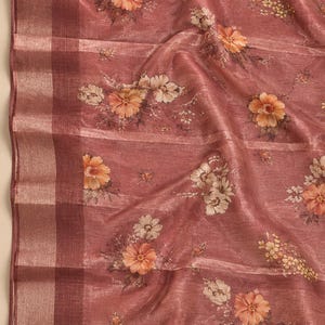 May include: A dusty rose fabric featuring a floral pattern with orange and cream-colored blossoms. The textile has a subtle sheen and a visible weave, with a wide, vertical border on the left side composed of alternating dark and light bands.