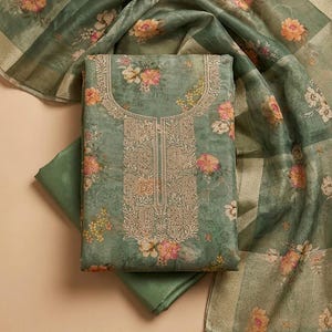 May include: A sage green fabric set featuring a floral print with pink and yellow blossoms. The central piece includes an intricate gold-toned embroidered neckline and front panel. A matching sheer, lightweight scarf with a floral pattern is included.