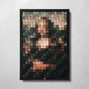 Puede incluir: Una obra de arte enmarcada que representa a la Mona Lisa, creada a partir de pequeños bloques de madera cuadrados en varios tonos de marrón, beige y negro. La obra está montada en un marco negro y cuelga de una pared blanca.
