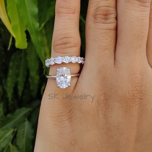 May include: A silver ring set with a large oval-shaped diamond and a smaller band of diamonds. The ring is on a person's finger.