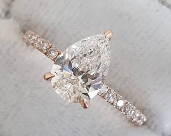 May include: A pear-shaped diamond engagement ring with a pave diamond band set in rose gold. The ring is displayed in a white velvet ring box.