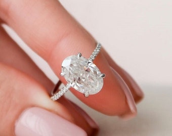 May include: A silver ring with a large oval-shaped diamond set in a pave setting. The ring is on a finger with pink nail polish.