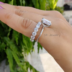 May include: A silver ring set with a large oval-shaped clear stone and a smaller band of clear stones. The ring is on a finger.