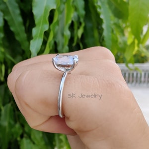 May include: A silver ring with a large, clear, oval-shaped gemstone. The ring is on a person's finger. The text "SK Jewelry" is visible on the ring.