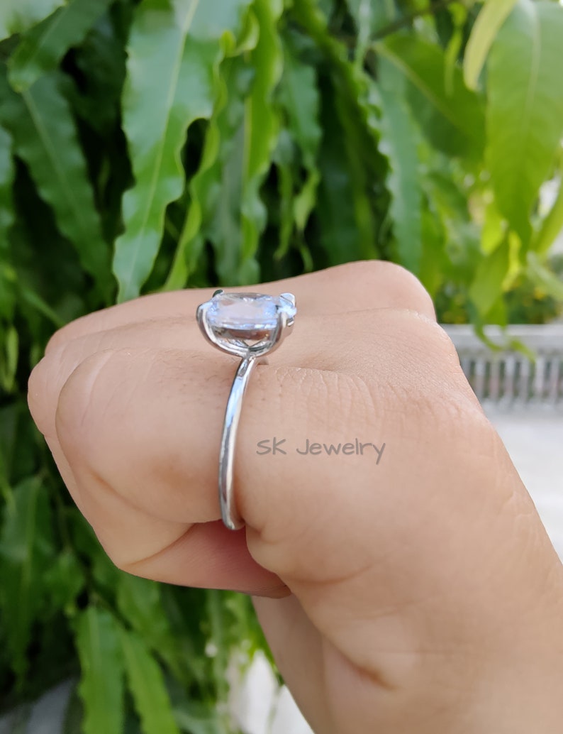 May include: A silver ring with a large, clear, oval-shaped gemstone. The ring is on a person's finger. The text "SK Jewelry" is visible on the ring.