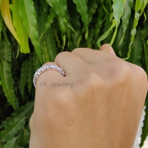 May include: A silver band ring with a row of clear round stones. The ring is on a person's finger.