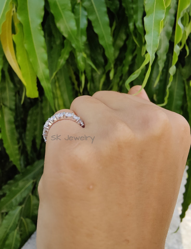 May include: A silver band ring with a row of clear round stones. The ring is on a person's finger.