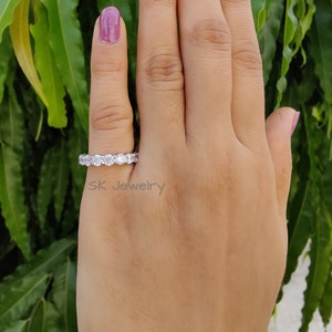 May include: A silver eternity band with a row of round, clear gemstones. The ring is on a person's finger.