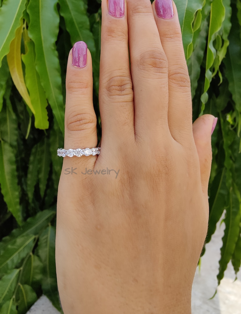 May include: A silver eternity band with a row of round, clear gemstones. The ring is on a person's finger.