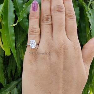 May include: A silver ring with a large oval-shaped clear gemstone. The ring is on a person's finger.