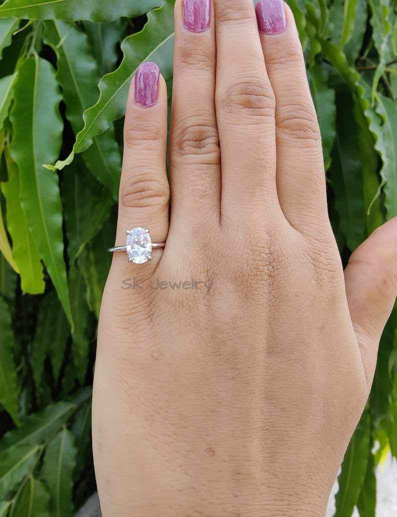 May include: A silver ring with a large oval-shaped clear gemstone. The ring is on a person's finger.