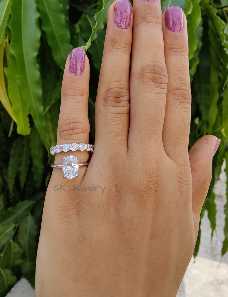 May include: A silver ring set with a large oval-shaped diamond and a smaller band of diamonds. The ring is on a person's finger.