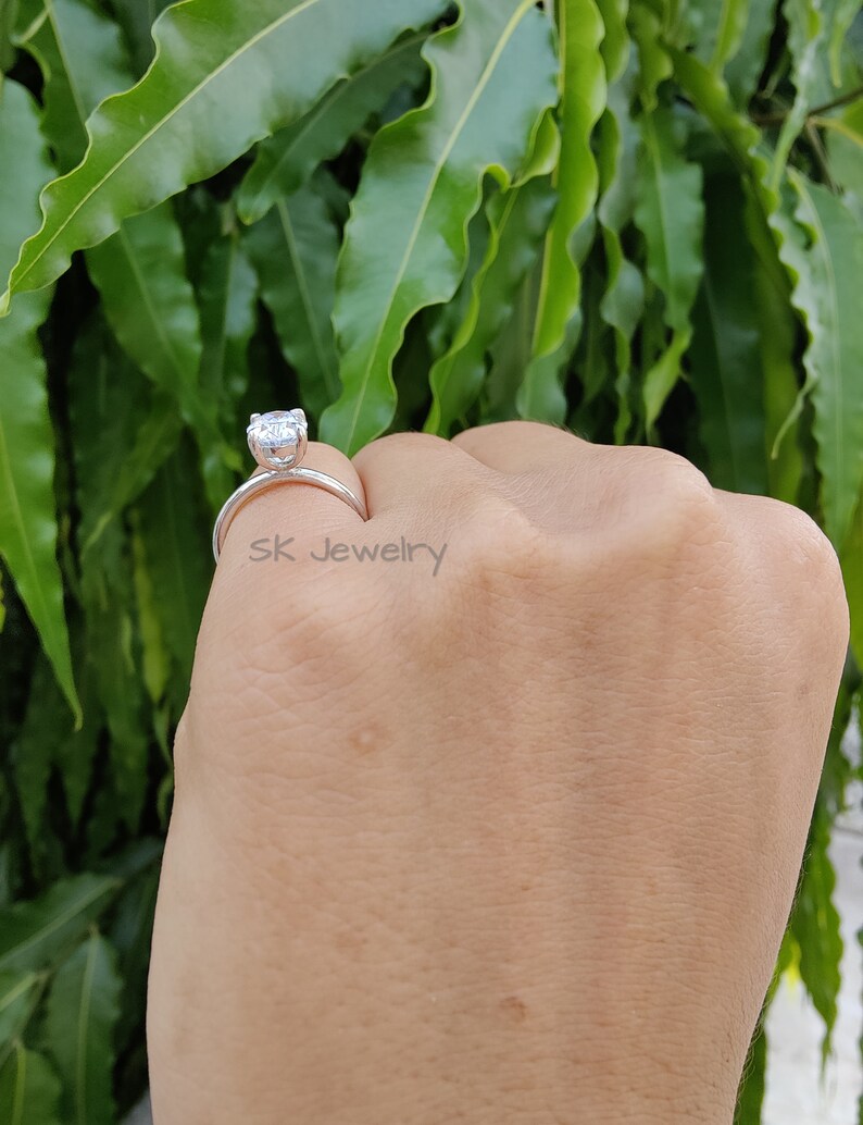 May include: A silver ring with a large, clear, round gemstone. The ring is on a person's finger. The text "sk jewelry" is visible on the ring.