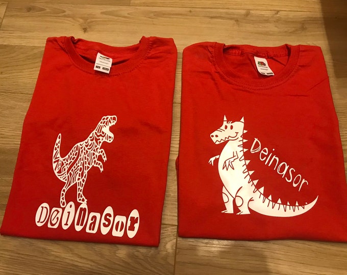 Crys T Deinasor i blentyn, a gellir ei bersonaleiddio a unrhyw enw/ Red kidsT shirt with Dinosaur image & can be personalised with any name.