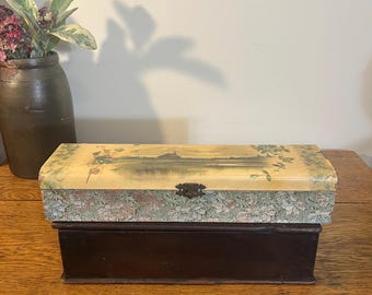 May include: An antique wooden box with a hinged lid. The lid features a landscape painting and floral patterned trim. The box is dark brown with a metal clasp. A decorative item for storage or display.