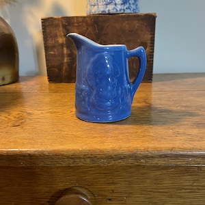 May include: A small blue ceramic creamer with a floral design. The creamer has a white interior and a handle.