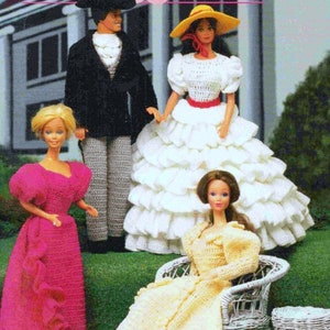 May include: Four crochet dolls dressed in vintage clothing. A doll in a black suit and a white shirt stands next to a doll in a white dress with a ruffled skirt. Two other dolls are seated, one in a pink dress and the other in a yellow dress.