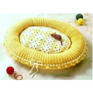May include: A yellow crocheted pet bed with a white crocheted centre. The bed is oval shaped and has a scalloped edge.