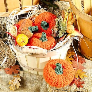 May include: A basket filled with crocheted pumpkins in shades of orange and green. The basket is made of woven wood and is sitting on a burlap surface.