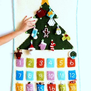 Könnte beinhalten: Ein gehäkelter Adventskalender in Form eines Weihnachtsbaums mit 23 nummerierten Taschen. Der Baum ist mit gehäkelten Ornamenten geschmückt, darunter ein Stern, ein Schneemann, ein Lebkuchenmann und ein Strumpf.