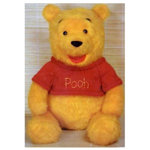 Op de afbeelding: Een pluche Winnie de Poeh beer die een rode trui draagt met het woord "Pooh" geborduurd op de voorkant.